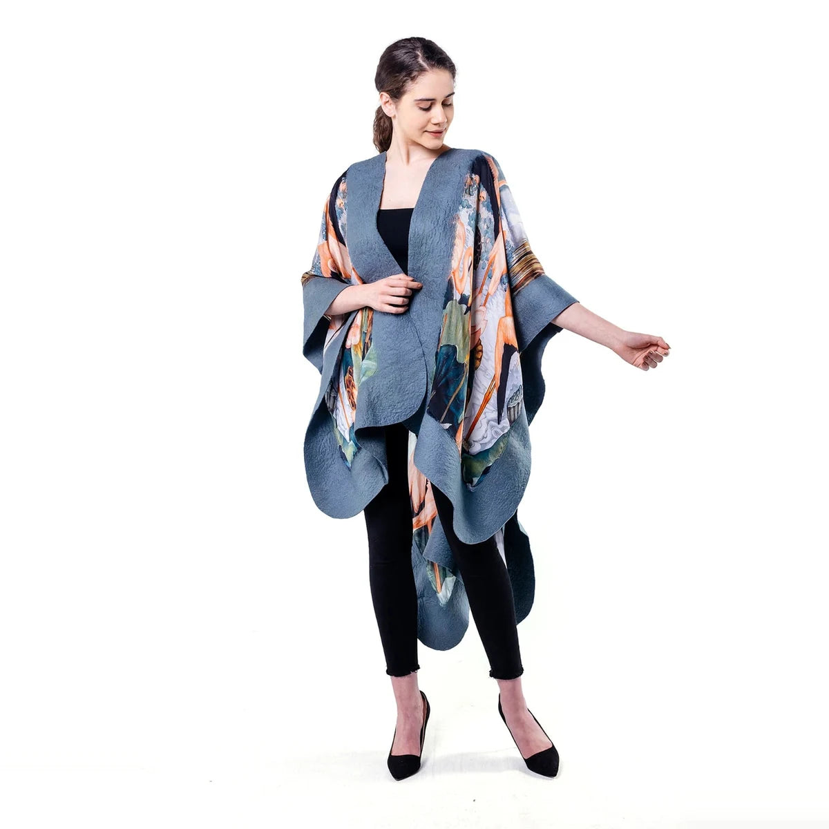 A woman modeling a blue-gray open-front poncho with a multicolor abstract print, worn over a black top and black leggings against a plain white background.